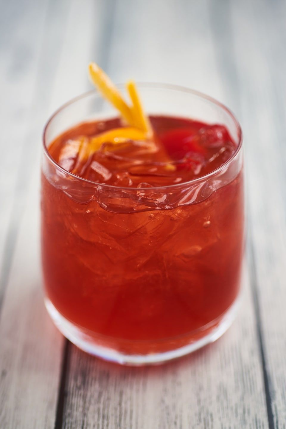 A red stirred cocktail over ice with an orange slice