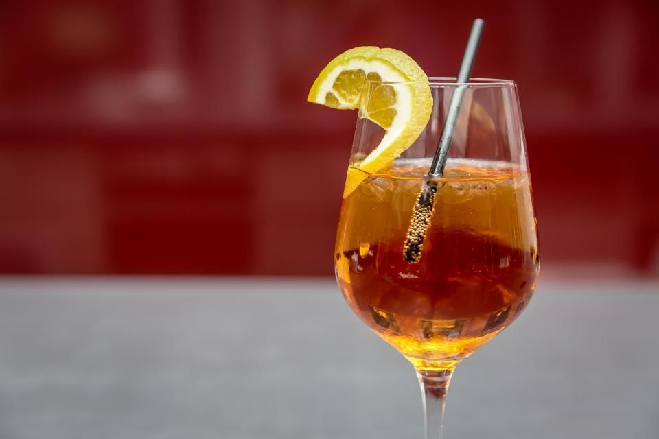 An amber spritz in a wine glass with a lemon wheel and a straw